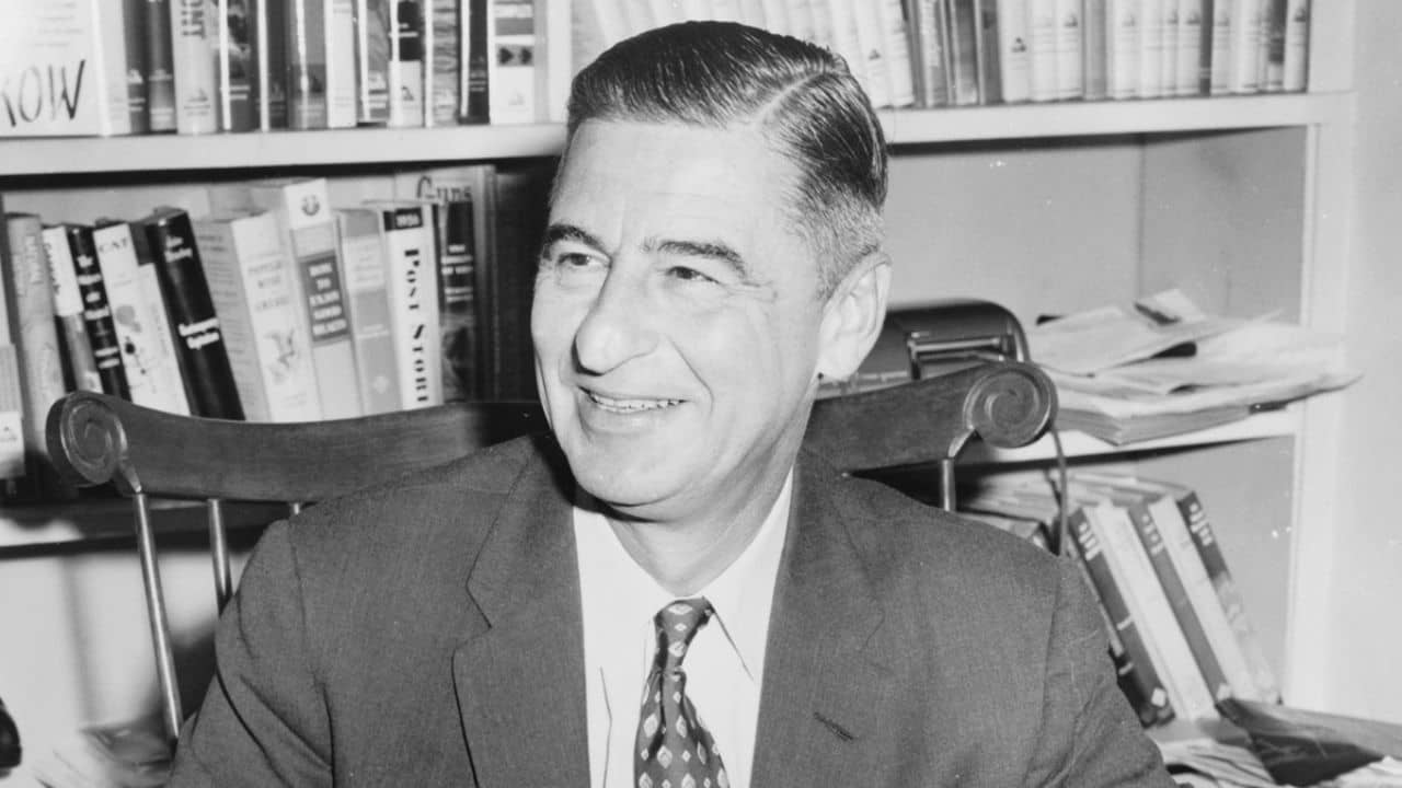 Ted Geisel (Dr. Seuss) half-length portrait, seated at desk covered with his books.