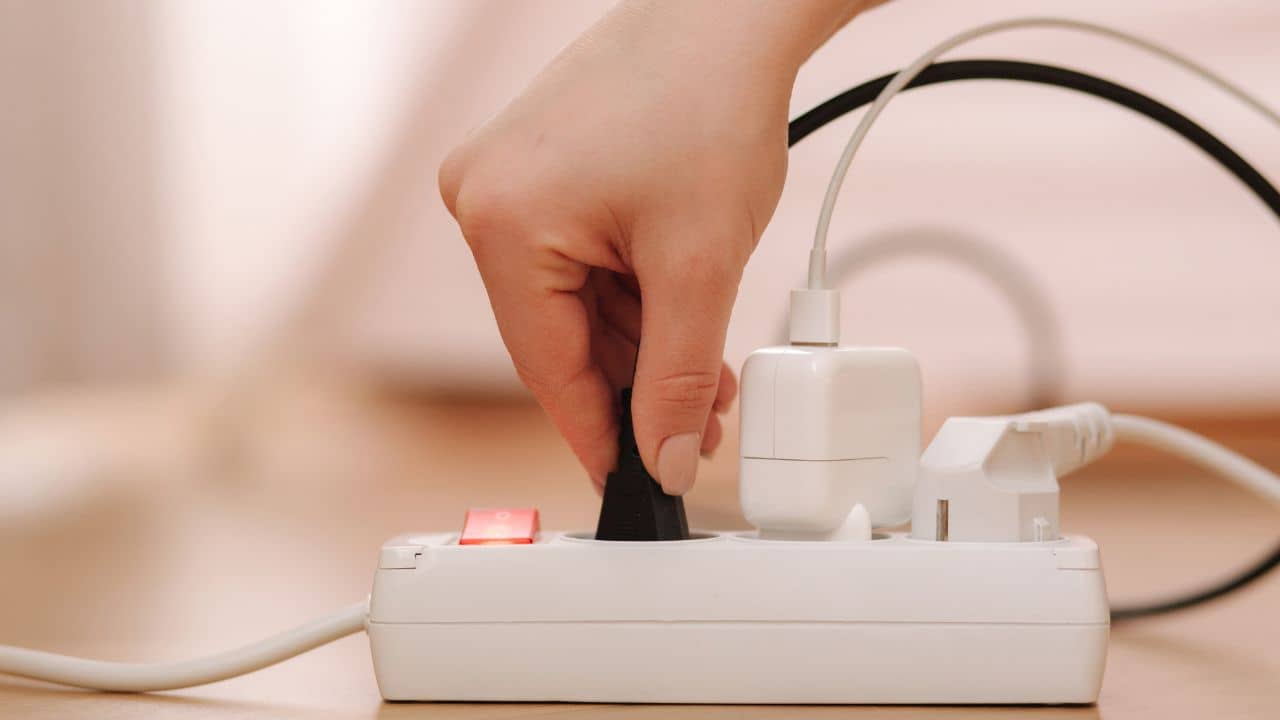 A Caucasian hand plugging in a power cord via an extension cord unit.