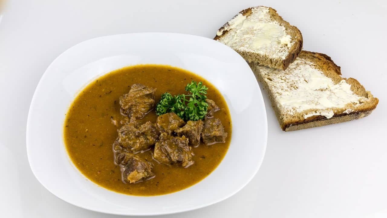 Oxtail soup with sliced bread, plated neatly on a white ceramic dish.