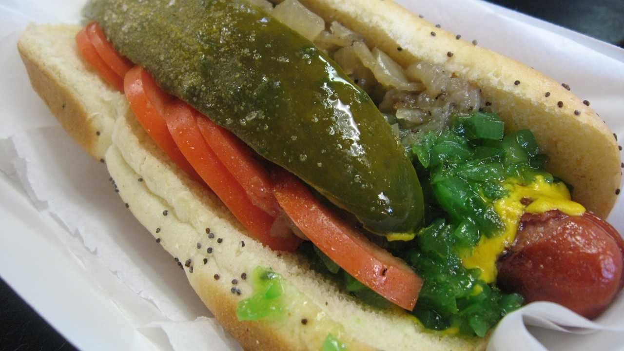 Close-up view of a Chicago-style hot dog complete with relish, mustard, tomato, peppers and more.
