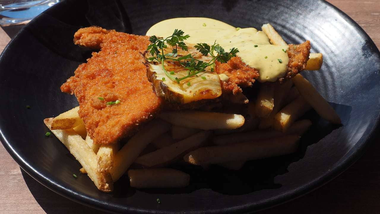 A Hawaiian schnitzel of pork with bearnaise sauce and fried pineapple, along with French fries and a glass of water, served for lunch at restaurant.