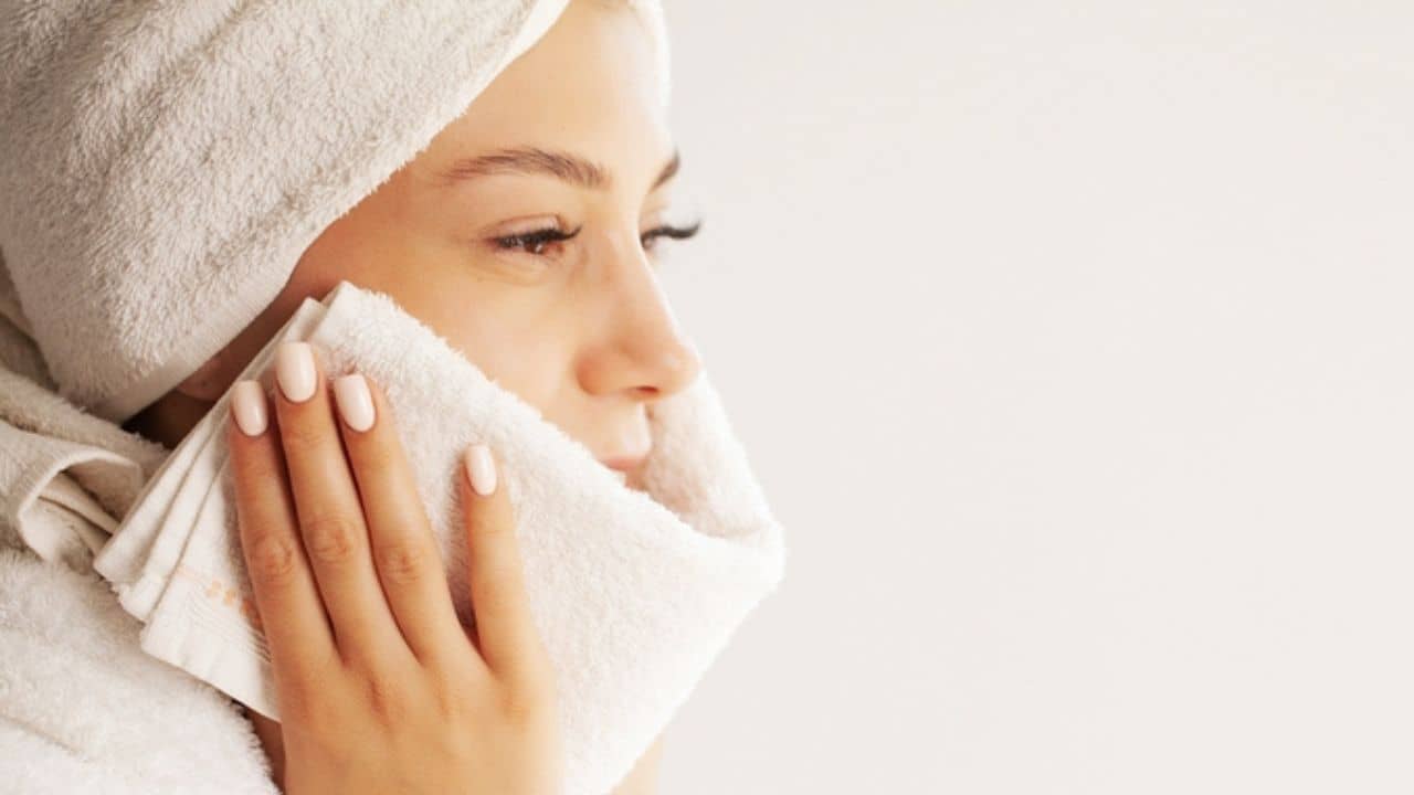 Young woman wiping her face with white towel after waking up in the morning
