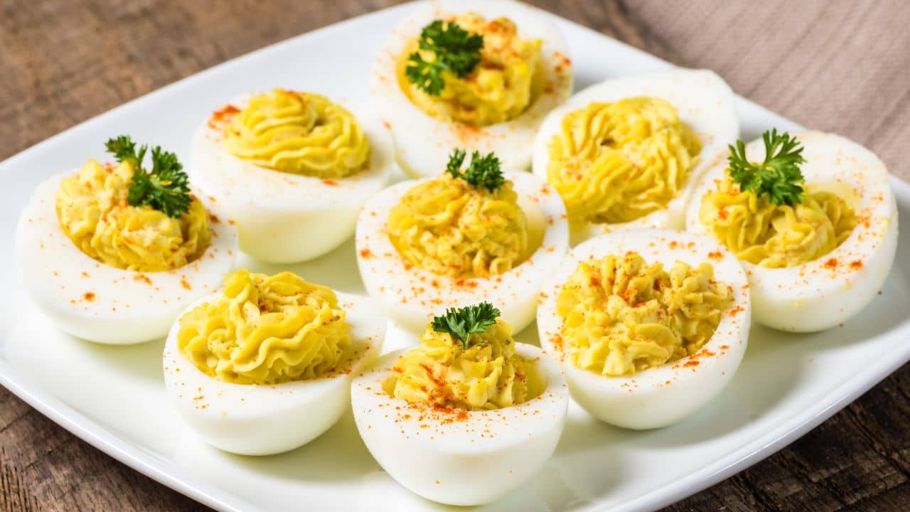 Traditional deviled eggs topped with paprika plated on a white ceramic dish.